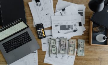 A Laptop Near the Dollars and Papers on a Wooden Table