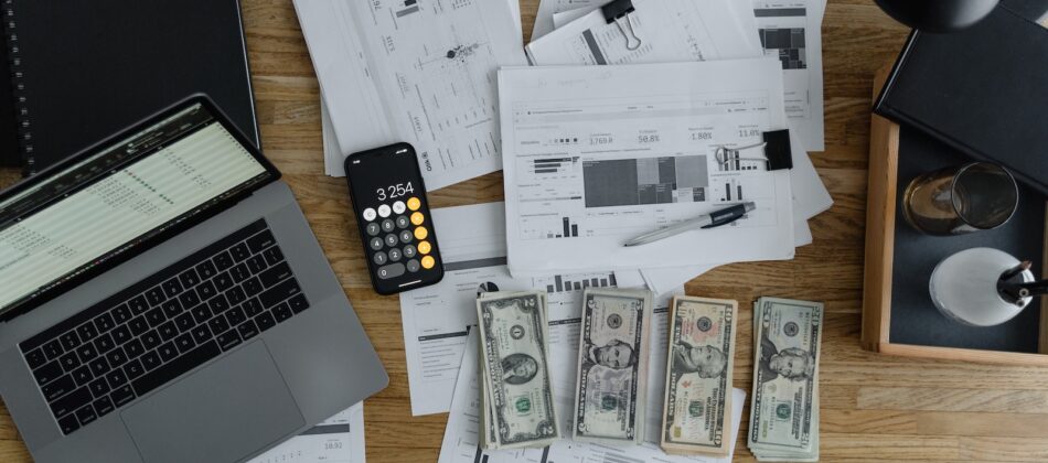 A Laptop Near the Dollars and Papers on a Wooden Table